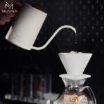 Tetera pour over MUVNA blanca de 600 ml vertiendo agua caliente en dripper blanco con café sobre jarra con hielo.