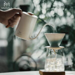Tetera pour over MUVNA blanca de 600 ml vertiendo agua sobre filtro de café en dripper blanco durante preparación manual