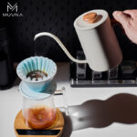 Tetera pour over MUVNA blanca de 600 ml vertiendo agua sobre filtro de café en dripper azul durante preparación manual.