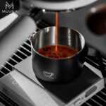 Taza para espresso 100 ml MUVNA, de acero inoxidable mate negro, en una sesión de preparación de café espresso, con el logo en la base.