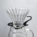 Dripper V60 de vidrio acanalado sobre la jarra decantadora, vista frontal en fondo gris